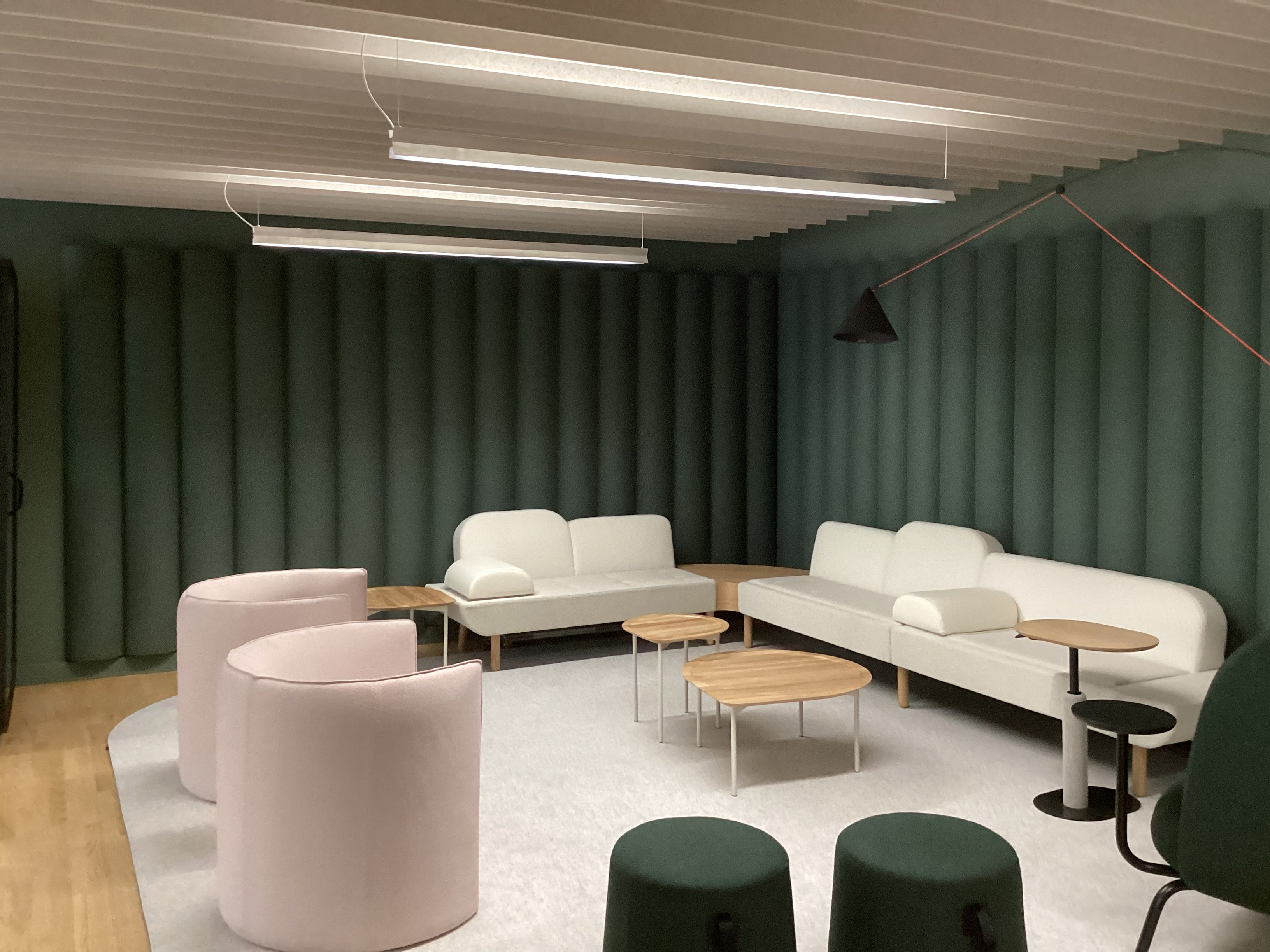 dark green acoustic tiles on wall behind sofas with beige rectangle baffles